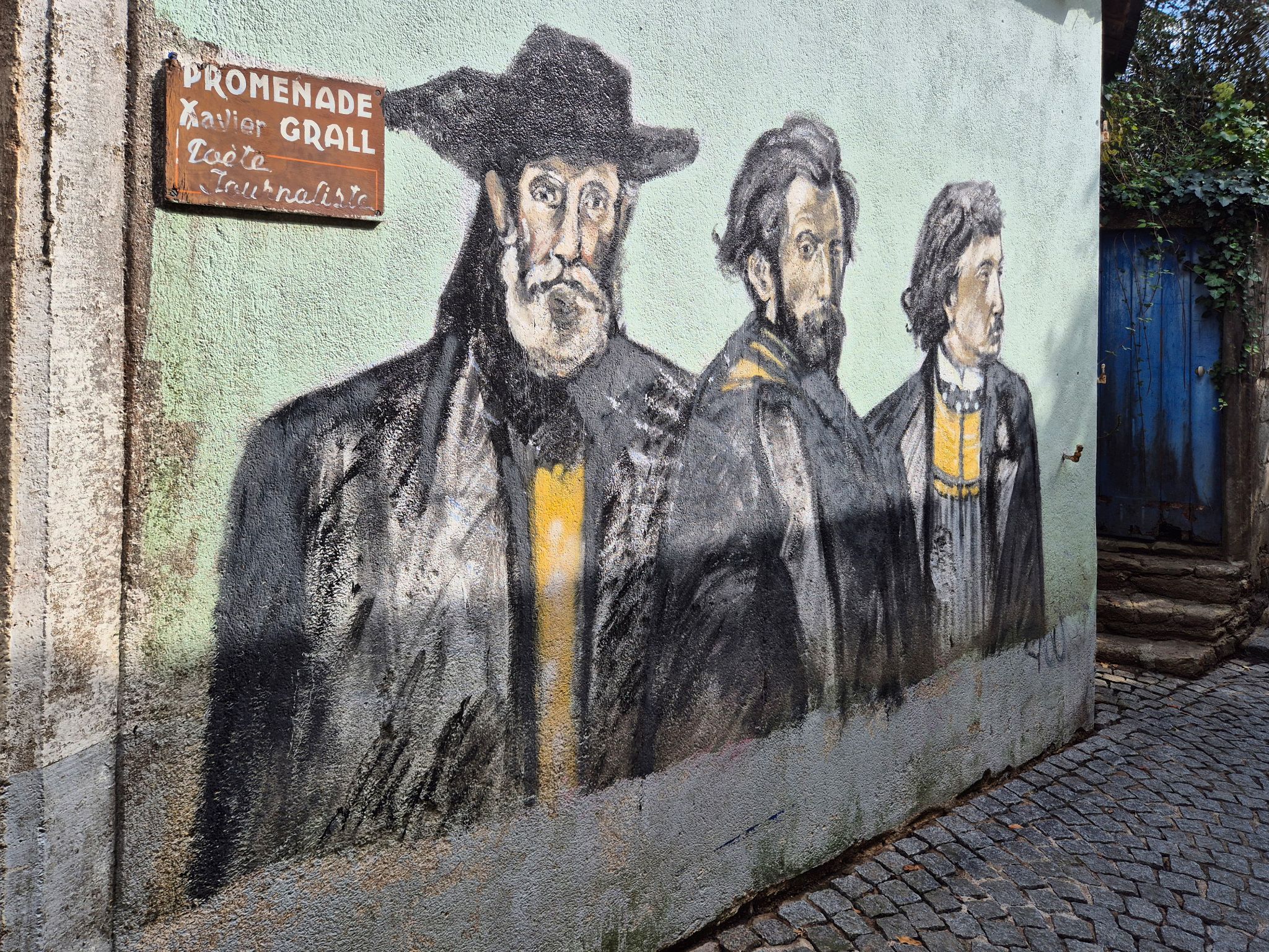 Das Wandbild zeigt drei prägende Persönlichkeiten der bretonischen Kultur: Xavier Grall, den engagierten Dichter und Journalisten; Théodore Botrel, den bekannten Chansonnier und Schriftsteller; sowie Jean-Pierre Calloc’h, den bretonischsprachigen Dichter und Priester, der im Ersten Weltkrieg fiel. Gemeinsam stehen sie für das kulturelle Erbe, das Pont-Aven und die Bretagne bis heute prägt.